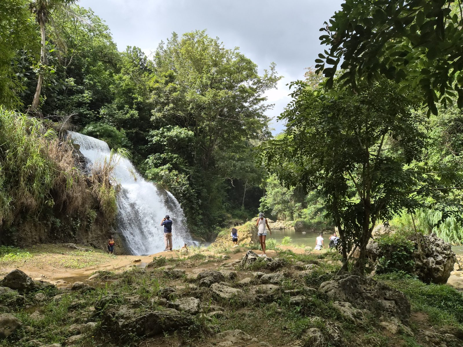 A waterfall at the edge of a green valley, with trees in the foreground