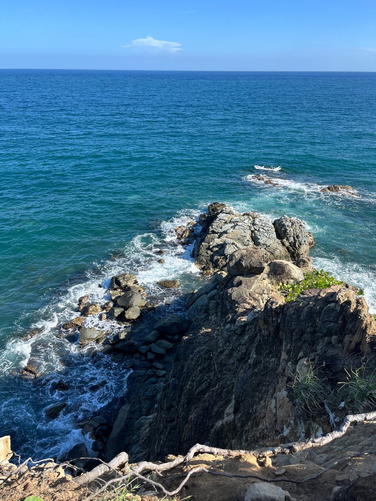 Waves breaking around a dark rock point in deep blue water